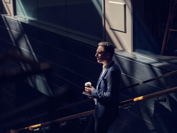 A man standing in a stairway with a cup of coffee in his hand A man standing in a stairway with a cup of coffee in his hand