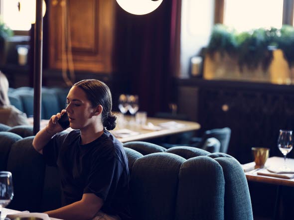 Ung kvinna som sitter på en restaurant och pratar i sin mobiltelefon Ung kvinna som sitter på en restaurant och pratar i sin mobiltelefon