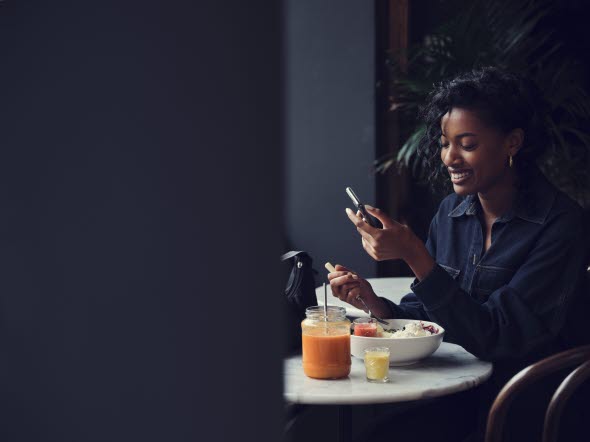 Young woman sitting at a breakfast table smiling and looking at her mobile phone Young woman sitting at a breakfast table smiling and looking at her mobile phone