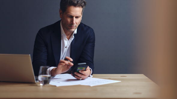 Man sitting in front of computer looking at his mobile phone