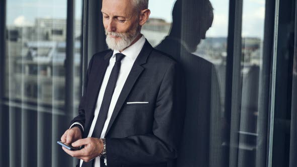 Picture of a man standing with his back against a window looking at his mobile phone