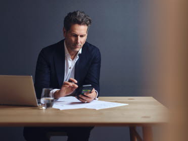 Man sitting in front of computer looking at his mobile phone
