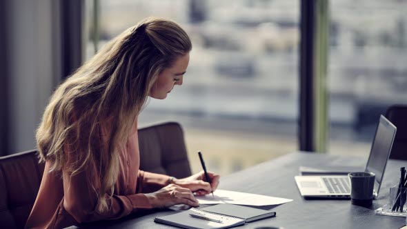 A woman sitting at a desk writing on a paper